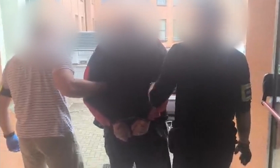 Dwaj funkcjonariusze prowadzą zatrzymanego mężczyznę zakutego w kajdanki.