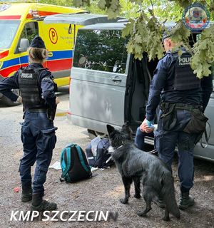 Dwoje policjantów z psem przy samochodzie, gdzie na podłodze siedzi mężczyzna.