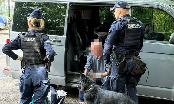 Dwoje policjantów z psem przy samochodzie, gdzie na podłodze siedzi mężczyzna.