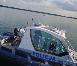 Łodzie ratunkowe na zbiorniku wodnym i wywrócona do góry dnem żaglówka.