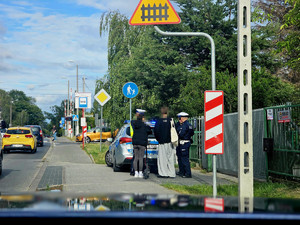 Trzej policjanci przy radiowozie rozmawiają z dwiema młodymi osobami.