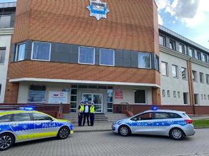 Przed budynkiem komisariatu stoją dwa radiowozy, oraz dwaj policjanci z mężczyzną.