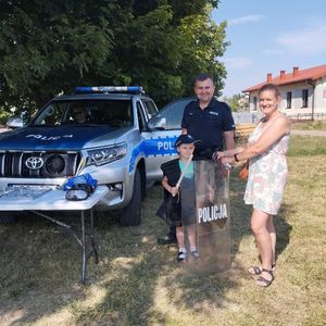 Policjant przy radiowozie pozuje do zdjęcia z uczestnikami festynu.