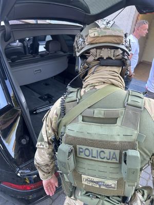 Policjant SPKP, przy otwartym bagażniku auta, w którym znajduje się broń.