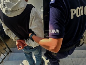 Policjant prowadzi zatrzymanego mężczyznę do samochodu.