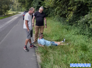 Dwaj mężczyźni nad jednym leżącym na poboczu.