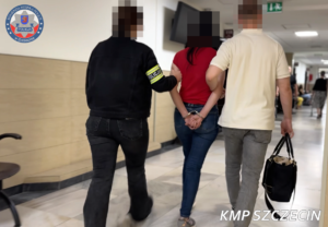 Dwaj funkcjonariusze prowadza zatrzymaną osobę korytarzem.