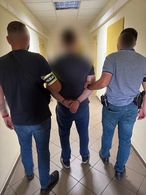 Dwaj policjanci prowadzą korytarzem zatrzymanego.