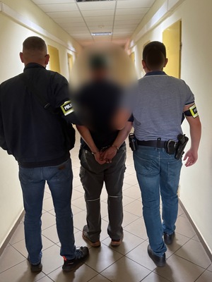 Dwaj policjanci prowadzą korytarzem zatrzymanego.