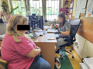 Zatrzymana kobieta i policjantka za biurkiem.