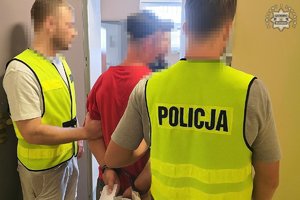 Dwaj policjanci w żółtych kamizelkach z napisem Policja prowadzą zatrzymanego.
