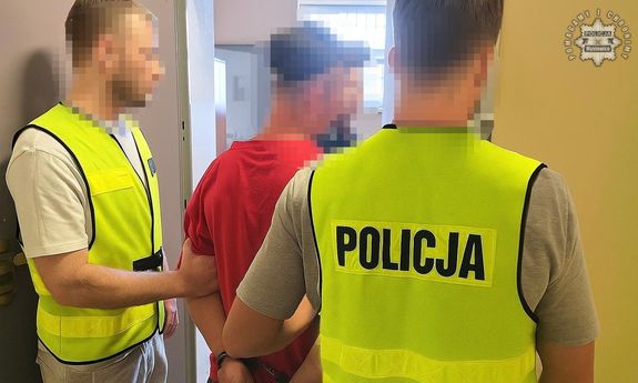 Dwaj policjanci w żółtych kamizelkach z napisem Policja prowadzą zatrzymanego.