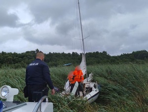 Policjant na policyjnej łodzi, i żaglówka, która utknęła w trzcinach.
