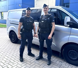 Dwaj policjanci stoją przy radiowozie policyjnym.