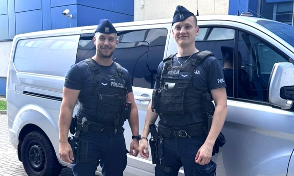 Dwaj policjanci stoją przy radiowozie policyjnym.