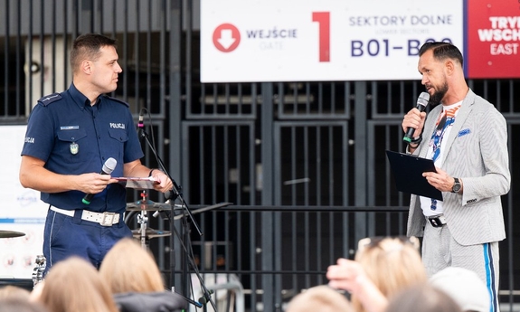 Policjant i mężczyzna razem na scenie. W dłoniach trzymają mikrofony.