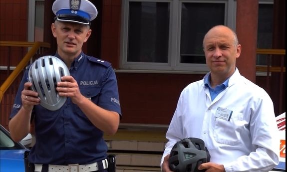 Policjant trzyma w ręku kask, obok stoi lekarz.