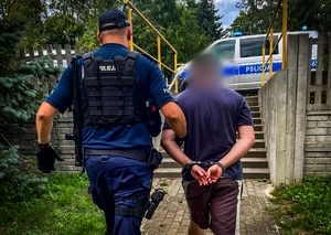 Policjant prowadzi zatrzymanego mężczyznę.