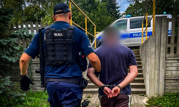 Policjant prowadzi zatrzymanego mężczyznę.
