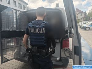 Policjant z zatrzymanym przy radiowozie.