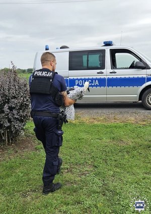 Policjant niesie bociana w kierunku radiowozu.
