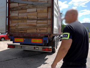 Otwarta paka samochodu wypełniona kartonami z nielegalnymi papierosami. Przed autem stoi policjant.
