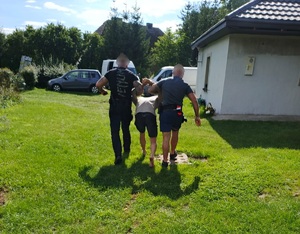 Dwaj funkcjonariusze prowadzą zatrzymanego.