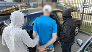 Dwaj funkcjonariusze prowadzą zatrzymanego mężczyznę.