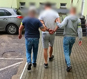 Dwaj funkcjonariusze prowadzą zatrzymanego mężczyznę.