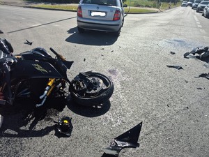 Miejsce wypadku. Na drodze leży uszkodzony motocykl, obok niego stoi samochód osobowy.