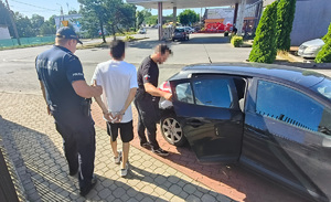 Funkcjonariusze prowadzą zatrzymaną osobę do radiowozu.