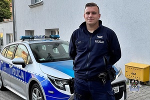 policjant stoi przed radiowozem.