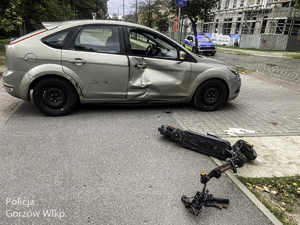 Hulajnoga leży obok uszkodzonego w zderzeniu samochodu.