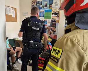 Policjant i strażacy oraz siedzący na krześle młody człowiek.