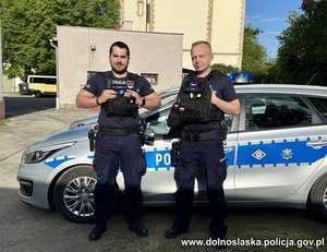 Dwaj policjanci stoją przy radiowozie policyjnym.