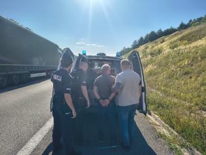 Policjanci z zatrzymanym przy pojeżdzie na drodze.