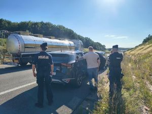 Policjanci z zatrzymanym przy pojeżdzie na drodze.