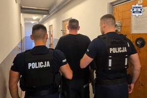 Dwaj funkcjonariusze prowadza zatrzymanego mężczyznę.