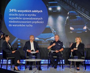 Uczestnicy inauguracji kampanii siedzą na krzesłach ustawionych na scenie. W tle na ekranie wyświetlany slajd.