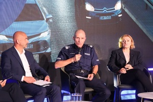 Uczestnicy inauguracji kampanii siedzą na krzesłach ustawionych na scenie. W tle na ekranie wyświetlany slajd. Wśród nich pierwszy zastępca komendanta głównego Policji mówi do mikrofonu.