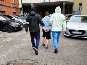 Dwaj policjanci prowadzą zatrzymaną kobietę.