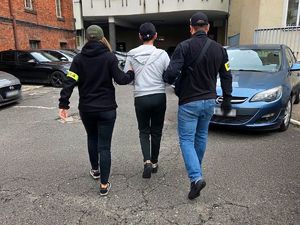 Dwaj policjanci prowadzą zatrzymaną kobietę.