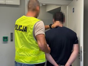 Funkcjonariusz prowadzi zatrzymanego w kajdankach.