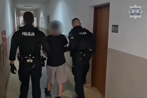 Dwaj policjanci prowadzą korytarzem zatrzymanego.