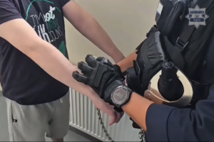 Policjant zakłada zatrzymanemu kajdanki zespolone.