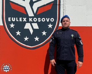 Policjant na tle herbu Eulex Kosowo.