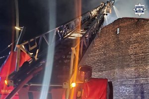 Drabina strażacka i lejąca się woda na dach budynku.