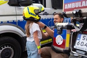 Policjant kuca przy dziewczynce zakładając jej na głowę kask.