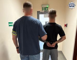 Nieumundurowany policjant trzyma zatrzymanego mężczyznę.