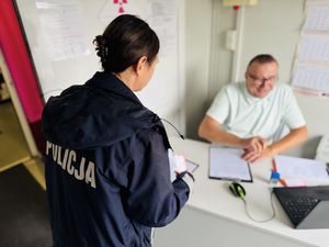 Policjantka przy stoliku, za którym siedzi ubrany na biało mężczyzna.